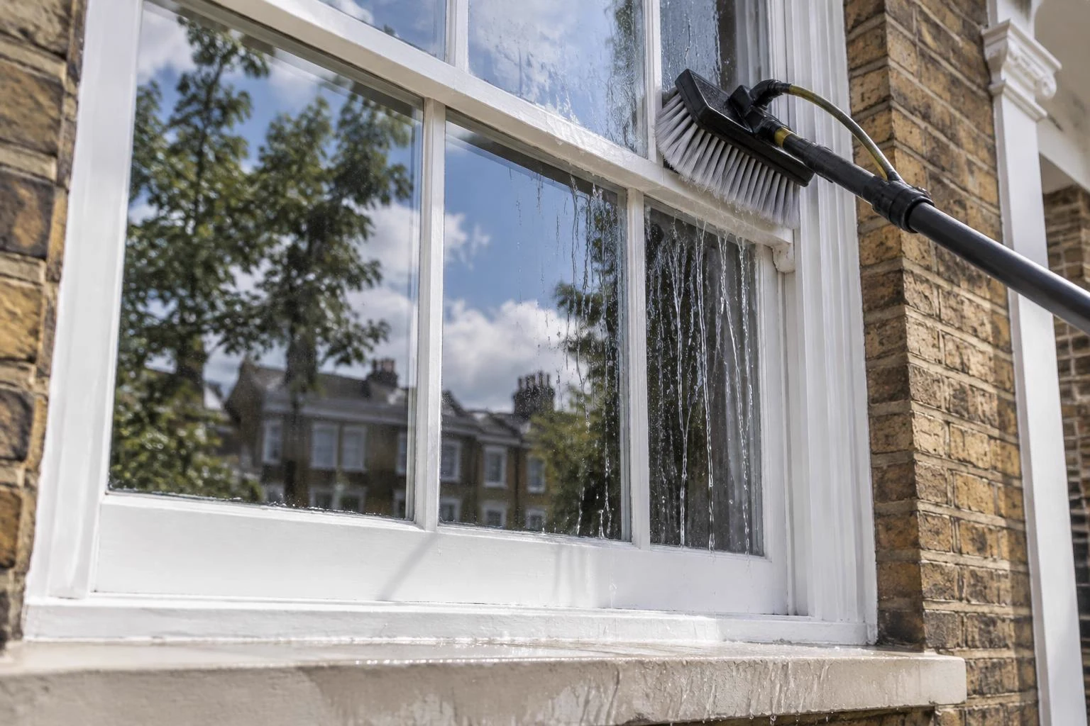 Soft brush and purified water cleaning the glass, frame and sill of a white timber sash window